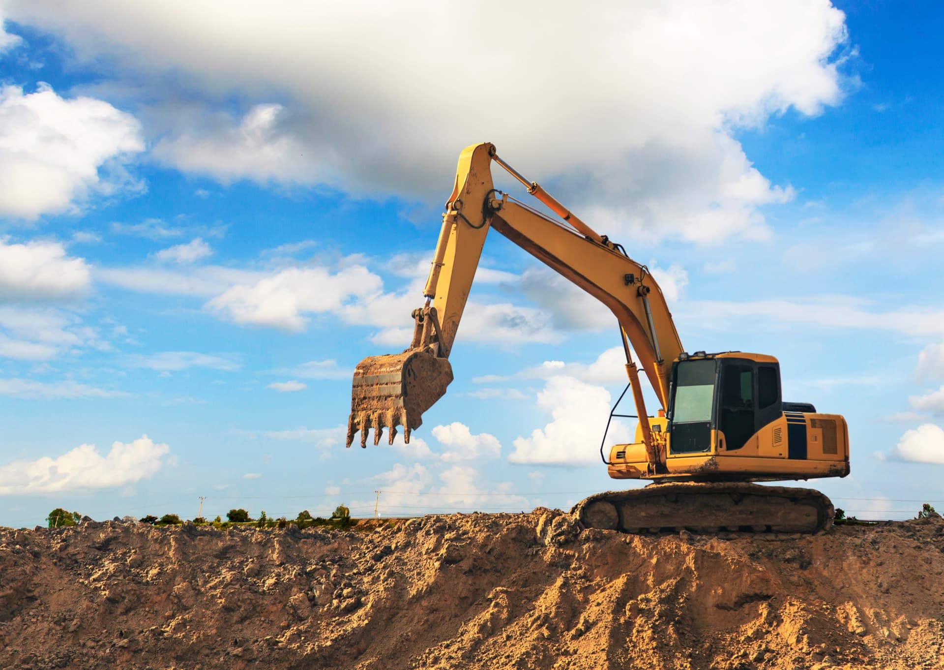 Bagger mit gehobenem Löffel auf einem Erdhügel vor blauem Himmel
